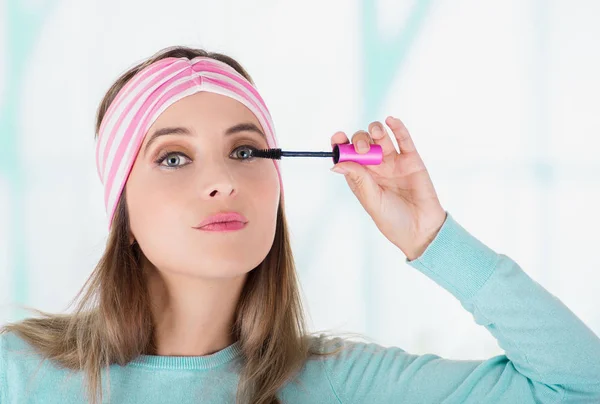 Primer plano de una hermosa joven usando un rímel en el ojo, en un fondo borroso — Foto de Stock