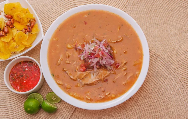 Vista superior de la comida tradicional ecuatoriana llamada Encebollado, estofado de pescado y cebollas anilladas en el interior, servido con palomitas de maíz, chifles, limón y salsa roja en el interior del tazón —  Fotos de Stock