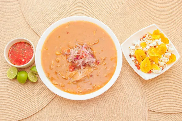 Vista superior de la comida tradicional ecuatoriana llamada Encebollado, estofado de pescado y cebollas anilladas en el interior, servido con palomitas de maíz, chifles, limón y salsa roja en el interior del tazón — Foto de Stock