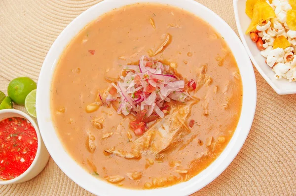 Acima da vista da comida tradicional equatoriana chamada Encebollado, guisado de peixe e cebola no interior, servido com pipoca, chifles, limão e molho vermelho dentro da tigela — Fotografia de Stock