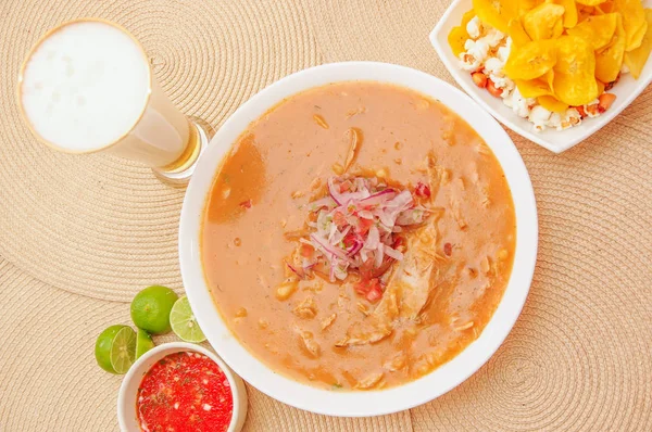 Vista superior de la comida tradicional ecuatoriana llamada Encebollado, estofado de pescado y cebollas anilladas en el interior, servido con palomitas de maíz, chifles, limón y vaso de cerveza con salsa roja en el interior del tazón —  Fotos de Stock