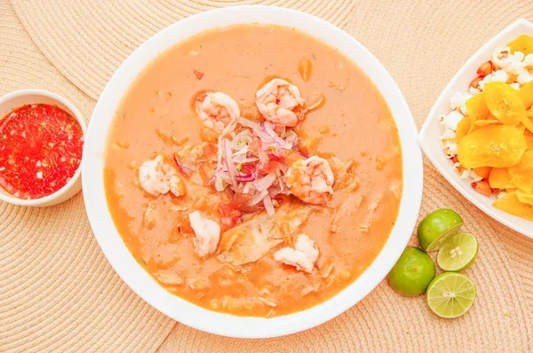 Vista acima da comida equatoriana: cebiche de camarão com alguns chifles dentro de tigela branca, limão e salada picante vermelha dentro de uma tigela branca em um fundo de mesa de madeira — Fotografia de Stock