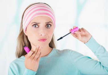 Close up of worried young woman doing a mess using a eye mascara in her eye, in a blurred background clipart