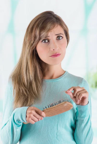 Close up of a gorgeous young woman doing a worried face while she brush her hair and taking the lost hairs from the brush, in a blurred background — Stock Photo, Image