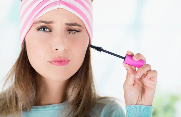 Close up of young woman, closing her eye while she is doing a mess using a eye mascara in her eye, in a blurred background — Stock Photo, Image