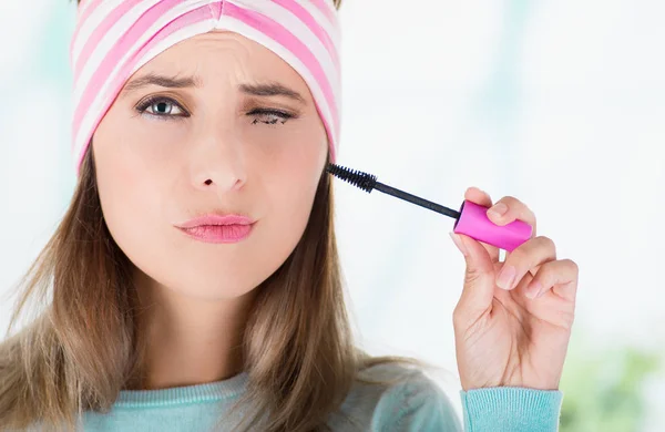 Primo piano di giovane donna, chiudendo l'occhio mentre sta facendo un pasticcio con un mascara occhio nell'occhio, in uno sfondo sfocato — Foto Stock