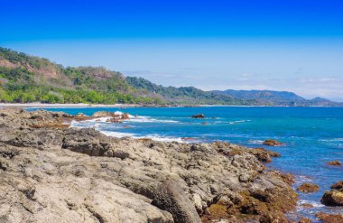 Güzel manzara Beach ile okyanus kaya oluşumları ile yaklaşan ve mavi gökyüzü kum ve orman yakınındaki dalgalar
