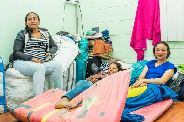 QUITO, ECUADOR, 21 de agosto de 2018: Mujeres no identificadas sentadas cerca de ropa, bolsos y accesorios en el suelo de una habitación dentro de un centro de refugio para personas que escapan de su país Venezuela —  Fotos de Stock