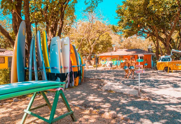 Tamarindo, Costa Rica, juni 26, 2018: utomhus utsikt över underbara kvinna promenader nära surfbräda presentbutik i solig dag och med blå himmel i avkopplande stranden i Tamarindo — Stockfoto