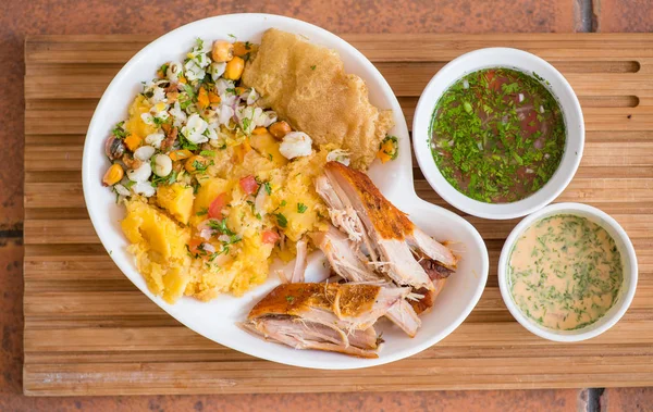 Oben Blick auf delikates Hornado mit Kartoffelpüree mit Salat, Tostado und Splitter in einem weißen Teller mit zwei kleinen Schüsseln mit grüner und rosa Sauce — Stockfoto