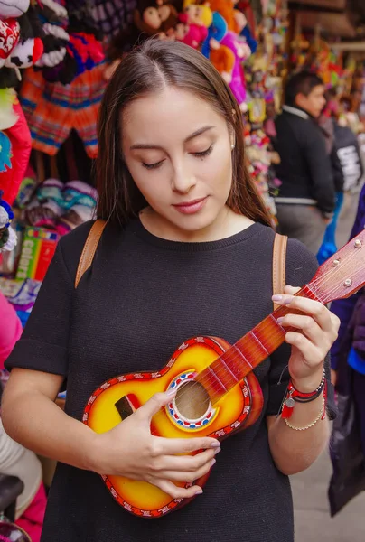 Close up of beautiful woman holding in her hands a small guitar and playing in a craft store in the Passage Craft in the downtown of the city of Banos — Stock Photo, Image