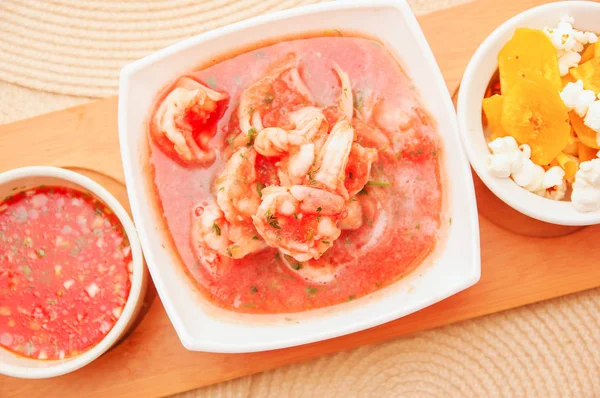 Di atas tampilan udang cebiche lezat dalam mangkuk putih persegi panjang disajikan dengan chifles dan saus pedas merah di atas struktur kayu di latar belakang meja — Stok Foto