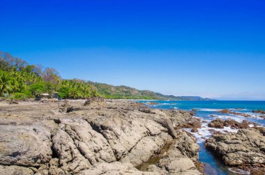 Beach ile okyanus kaya oluşumları ile güzel manzara mavi gökyüzü içinde Playa Montezuma, Kosta Rika ile yaklaşan ve mavi gökyüzü kum ve muhteşem mavi gökyüzü ve güneşli bir gün ormanda yakınındaki dalgalar