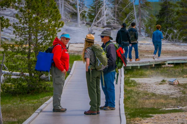 오래 된 충실 한 어퍼 간헐천 분 지에 나무 경로 통해 여성 공원 레인저와 얘기 하는 미확인된 관광객의 옐로스톤, 몬태나, 미국 2018 년 5 월 24 일: 야외 보기 — 스톡 사진