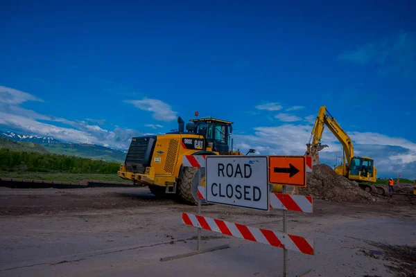 PARC NATIONAL YELLOWSTONE, WYOMING, ÉTATS-UNIS - 07 JUIN 2018 : Panneau informatif de la fermeture de la route avec équipement stationné dans une zone de construction dans le parc national Yellowstone — Photo