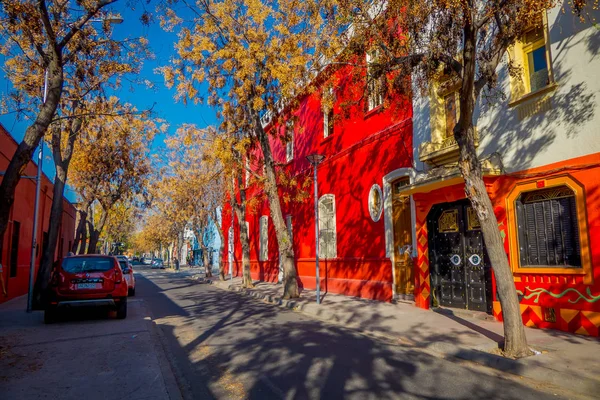 САНТЬЯГО, ЧИЛЬ - 13 СЕНТЯБРЯ 2018 г.: Автомобили, припаркованные под деревьями на одной стороне улицы в Баррио Юнгай с красной строительной стеной в Сантьяго — стоковое фото
