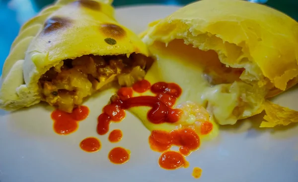 Nahaufnahme von selektivem Fokus chilenischer Empanadas in zwei Stücken mit köstlichem geschmolzenem Käse und Schinken, fotografiert mit natürlichem Licht über einem weißen Teller — Stockfoto