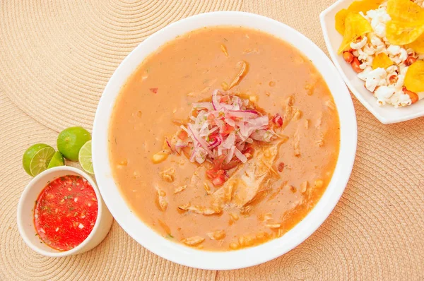 Vista superior de la comida tradicional ecuatoriana llamada Encebollado, estofado de pescado y cebollas anilladas en el interior, servido con palomitas de maíz, chifles, limón y salsa roja en el interior del tazón —  Fotos de Stock