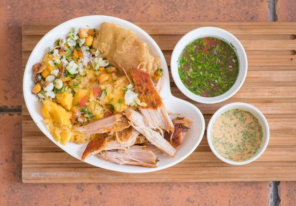 Boven weergave van lekker hornado met aardappelpuree met salade, tostado en mote binnenkant van een witte plaat met twee smalls kommen met groen en roze saus — Stockfoto