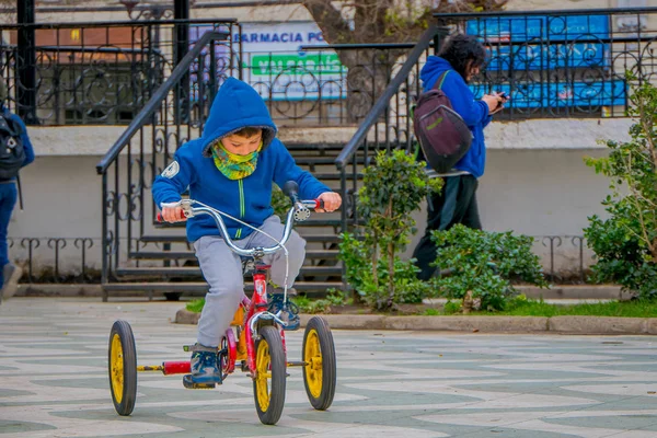 VALPARAISO, CHILE - SEPTIEMBRE, 15 de septiembre de 2018: Vista al aire libre del niño no identificado que lleva chaqueta azul para el clima frío y monta su triciclo en una plaza de un parque ubicado en el centro de Valparaíso —  Fotos de Stock
