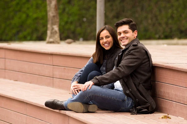 Primer plano de una hermosa joven pareja sonriente enamorada en San Valentín y mirando a la cámara, sentada en un parque — Foto de Stock