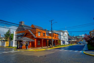 PUERTO VARAS, CHILE, SEPTEMBER, 23, 2018: Outdoor view of beautiful wooden building in the corner with some cars aproaching in a sunny day with blue sky background located in Puerto Varas in Chile clipart