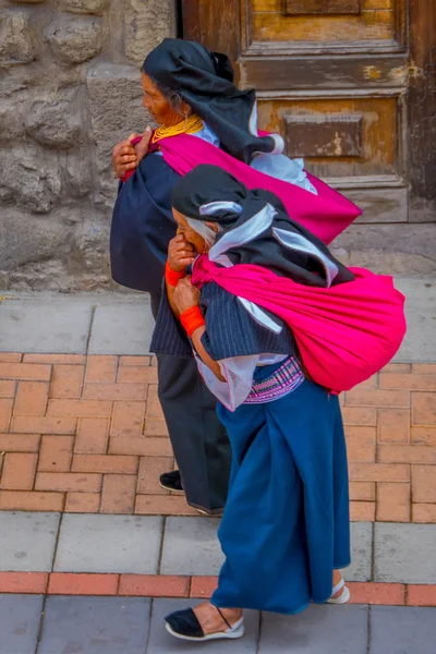 COTACACHI, ECUADOR, 06 DE NOVIEMBRE DE 2018: Vista al aire libre de dos mujeres indígenas caminando juntas por las calles de Cotacachi y sosteniendo en sus maletas de ropa en la ciudad de Cotacachi — Foto de Stock