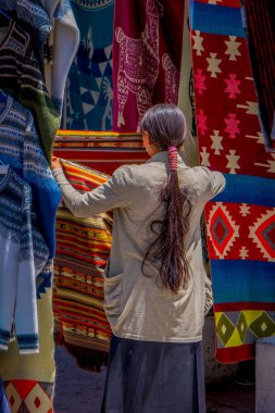 And geleneksel giyim ve Otavalo şehir sokak pazarında bazı ürünleri satan giyen yerli kadın arkadan görünüm