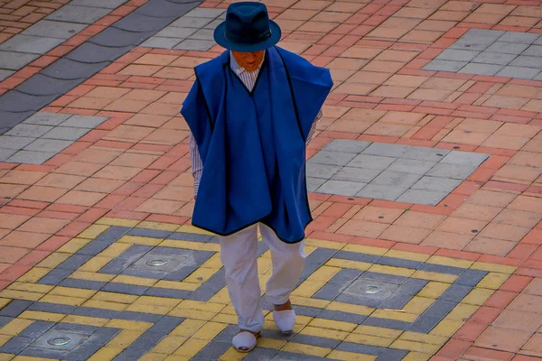 COTACACHI, ECUADOR, 06 DE NOVIEMBRE DE 2018: Anciano no identificado con ropa indígena, pantalones y zapatos blancos, sombrero azul y chaleco y caminando por la acera de la ciudad de Cotacachi — Foto de Stock