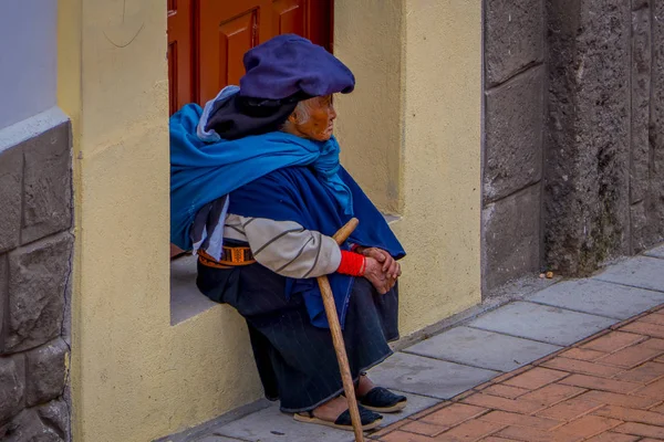 COTACACACHI, ECUADOR, NOVEMBER 06, 2018: Outdoor view of old indigenous woman sitting in the border of a house in Cotacachi — стоковое фото