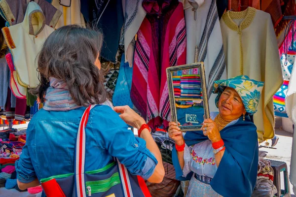 OTAVALO, ECUADOR, NOVEMBER 06, 2018: Close up of hispanic indigenous woman holding a mirror for customers prove their clothes in a street market in Otavalo — Stock Photo, Image