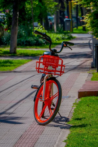 SANTIAGO, CHILE - SEPTEMBER 13, 2018: Red bike parked at one side of the sidewalk inside of a park located in the city of Santiago of Chile during gorgeous beautiful sunny day — Stock Photo, Image