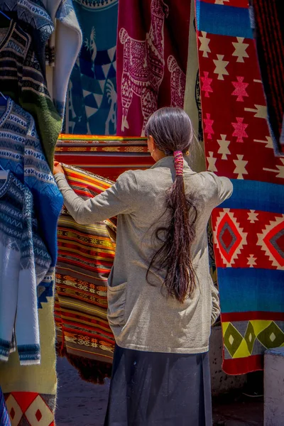 OTAVALO, ECUADOR, 06 DE NOVIEMBRE DE 2018: Vista posterior de una mujer indígena vestida con ropa tradicional andina y vendiendo algunos productos en el mercado callejero de la ciudad de Otavalo — Foto de Stock