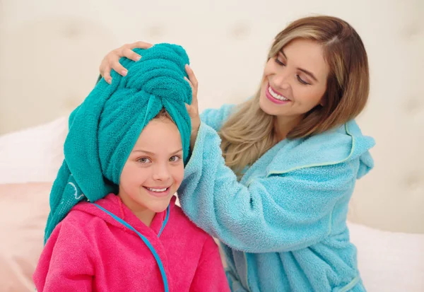 Cxlose upp av ung mamma aplying till hennes lilla dotter en blå handduk i huvudet medan båda bär en badrockar — Stockfoto