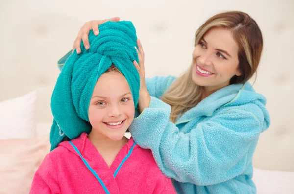 Cxlose się młoda Mama aplying do jej córeczkę niebieski ręcznik w głowie, gdy oba są sobie szlafroki — Zdjęcie stockowe