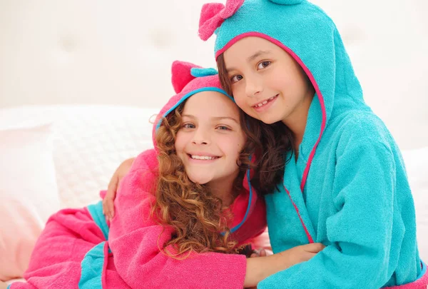 Retrato ou duas irmãs abraçando um ao outro e vestindo toalhas de banho com capuz — Fotografia de Stock