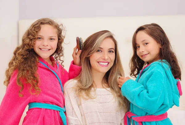 Nahaufnahme von zwei kleinen Mädchen, die mit den Haaren ihrer Mutter spielen, während lockige Mädchen ein rosa Bademantel und brünettes Mädchen ein blaues Bademantel tragen — Stockfoto