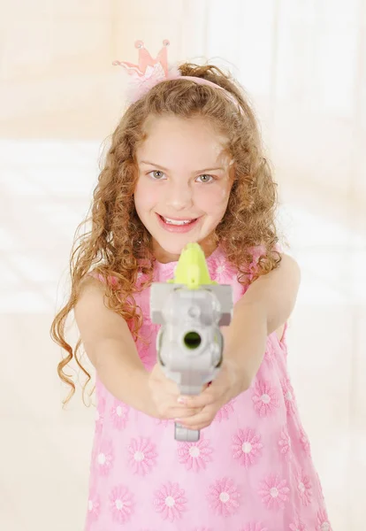 Glückliches kleines Mädchen, das eine Waffe richtet und ein rosafarbenes Prinzessinnenkleid trägt — Stockfoto