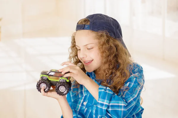 Nahaufnahme eines schönen lockigen Mädchens, das Jungenkleidung mit Hut trägt und ein Autospielzeug in der Hand hält — Stockfoto