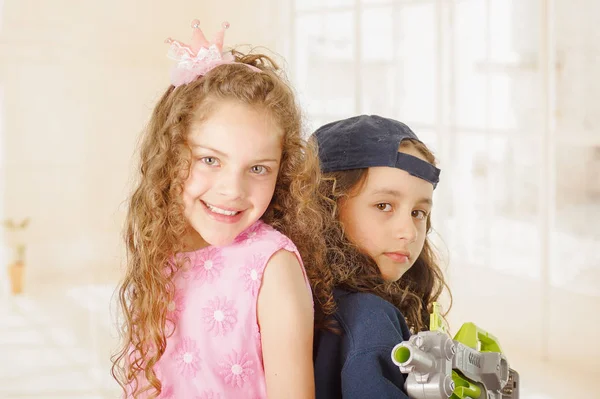 Primer plano de dos chicas una es wering ropa de niño y la celebración de un arma y otra chica está usando un vestido de princesa rosa —  Fotos de Stock