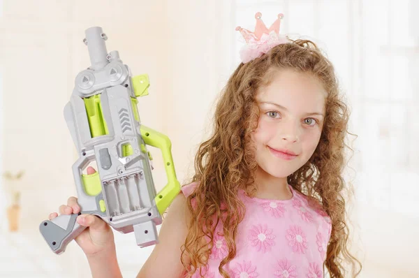 Närbild på vackra lockiga flicka wearin pojke kläder och håller i hennes händer en leksakspistol — Stockfoto