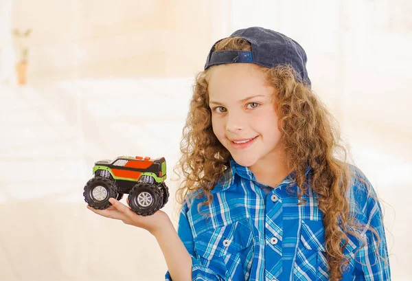 Close up of beautiful curly girl wearing boy clothes with hat and holding a car toy in her hand — Stock Photo, Image