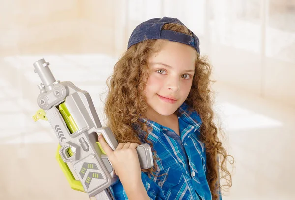 Закрывая красивую кудрявую девочку в одежде мальчика и держа в руках игрушечный пистолет — стоковое фото