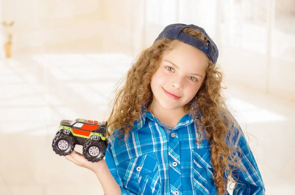 Close up van mooi krullend meisje dragen jongen kleding met hoed en een speelgoed auto houdt in haar hand — Stockfoto