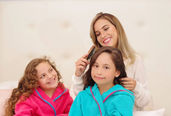 Nahaufnahme einer jungen Mutter, die ihrer kleinen Tochter die Haare streift, die ein blaues Badetuch trägt, während ihr anderes lockiges Mädchen auf ihren Zug wartet — Stockfoto