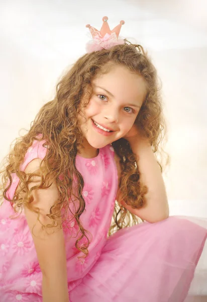 Beautiful little curly girl posing for camera and wearing a pink princess dress