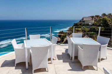 White tables and chairs at a outdoor cliff cafe with ocean view, Ungasan, Bali, Indonesia. clipart