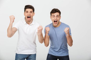 Fotoğraf iki kendinden geçmiş erkek 30'lu rahat t-shirt ve bağırarak ve beyaz arka plan üzerinde izole yumruk kenetlenmesi ile zafer sevindirici kot giyen