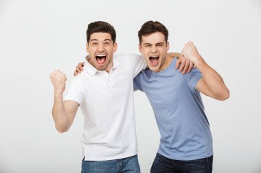 Fotoğraf iki neşeli erkek 30'lu rahat t-shirt ve sarılma ve beyaz arka plan üzerinde izole yumruk kenetlenmesi ile bağırarak kot giyen