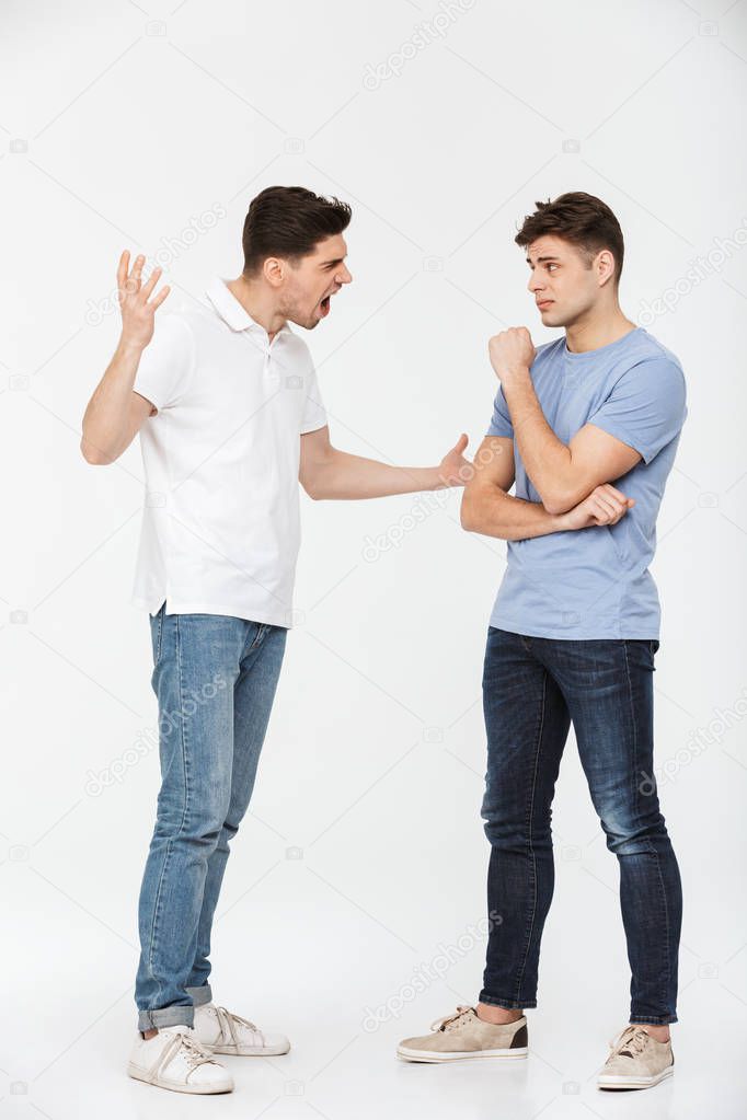 Full length portrait of two angry young men arguing isolated over white background